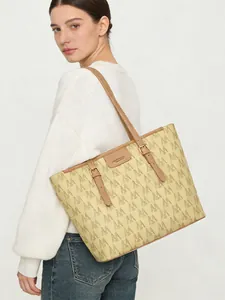 Detalle del bolso tote grande con monograma y correas de cuero marrón llevado por una modelo