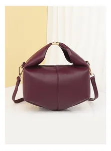 Detail of burgundy lychee leather handbag showing golden clasp and geometric fold structure