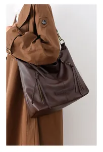 Close-up of dark brown pebbled leather tote bag with dual zippers worn with trench coat