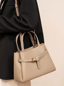 Minimalist taupe lychee leather tote bag shown on model with elegant gold buckle detail