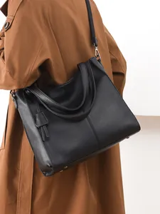 Black pebbled leather tote bag with wide canvas strap shown on model in brown trench coat