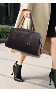 Detalle del bolso tote de cuero marrón con colgante dorado y elegantes costuras en contraste