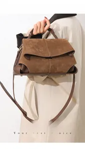 Detail of matte suede and smooth leather texture on a dark brown handbag with metal feet