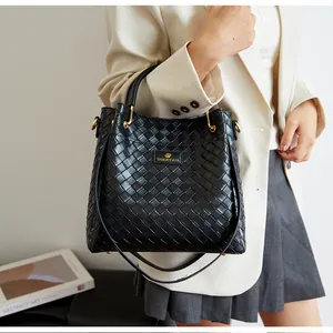 Gros plan sur un sac seau noir en cuir tressé avec logo métallique et détails dorés