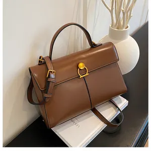 Sac à main en cuir marron avec boucle dorée posé sur un livre blanc décoratif