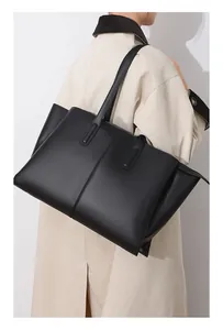 Detail of a large matte black tote bag with gold zipper worn with a beige trench coat