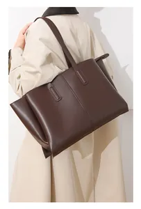 Detailed side view of a large coffee brown leather tote bag worn with a beige trench coat