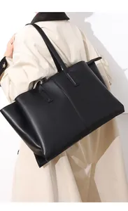 Detail view of black leather tote bag with gold zipper and vertical stitching on beige trench