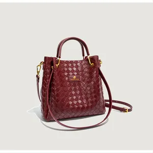 Gros plan sur la texture tressée bordeaux et les détails dorés d'un sac seau chic