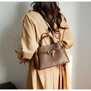 Detail of dark brown woven tote bag with adjustable shoulder strap and gold buckle accent