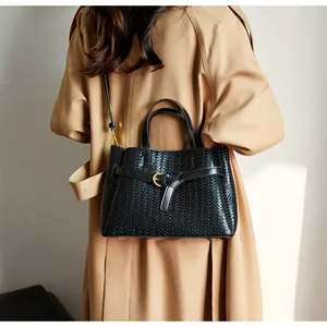 Detail of black woven tote bag with gold hardware worn over a khaki trench coat
