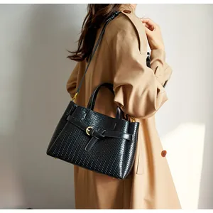 Close-up of black woven tote bag with gold buckle on a model in a beige trench coat
