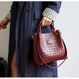 Gros plan sur la texture en cuir tressé bordeaux et le logo de ce sac seau chic