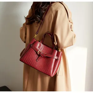 Detail of burgundy woven tote bag worn by a model in a beige trench coat for a stylish look