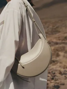 Elegante bolso bandolera de media luna en cuero beige granulado llevado por una modelo