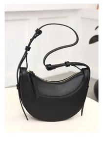 Detalle del bolso de media luna negro con textura cruzada y acabados metálicos dorados