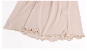 Detail of the light beige silk nightdress featuring a delicate ruffled lettuce edge hemline