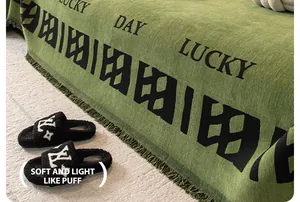 Détail macro du jeté de canapé en chenille verte avec texte Lucky Day et franges