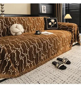 Dettaglio del copridivano in ciniglia marrone scuro con jacquard bianco e nappe