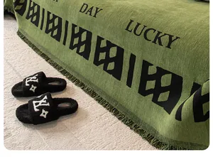 Détail de chaussons en fausse fourrure noire avec logo blanc sur un plaid tricoté vert