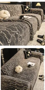 Dettaglio del copridivano in maglia grigia geometrica con texture jacquard e frange