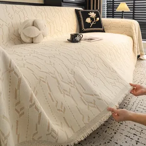 Copridivano in maglia color crema con motivo geometrico e nappe decorative