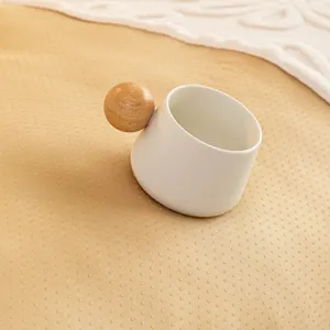 Minimalist white ceramic cup with a spherical wooden handle on a warm fabric background