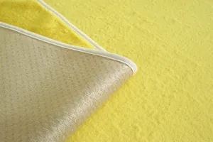 Détail d'un tapis en peluche jaune montrant la fourrure douce et le dos antidérapant