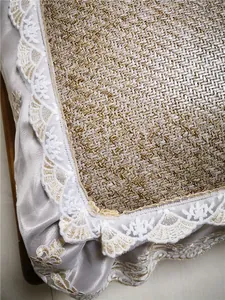 Detailed close-up of woven rattan summer mat with delicate silver lace trim and floral embroidery