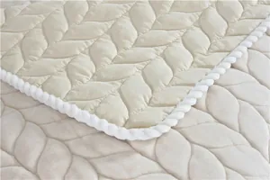 Detailed macro view of beige quilted plush rug with leaf patterns and braided rope edge