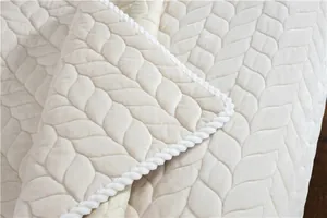 Close-up of beige plush rug featuring leaf quilted texture and white braided edge trim
