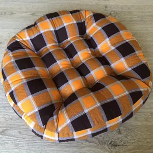 Detail of round orange checkered floor cushion with quilted tufted texture on wood floor