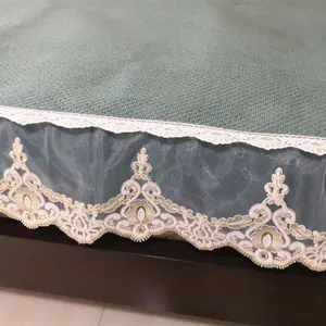 Detail of grey-green waffle texture fabric with golden embroidery lace and blue mesh