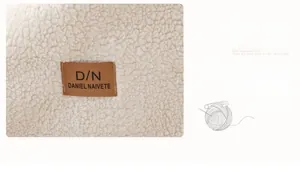 Détail de la housse de canapé en laine d'agneau blanc cassé avec écusson en cuir marron