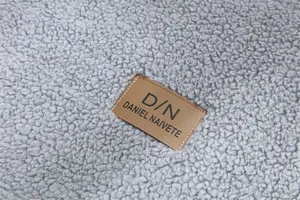 Détail du coussin de canapé en laine d'agneau grise avec logo de marque en cuir brun