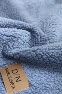Détail d'un jeté de canapé en polaire bleu doux avec une étiquette en cuir marron