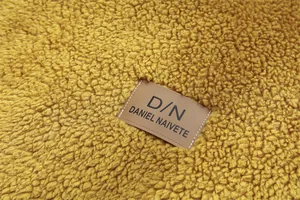 Détail macro du tissu polaire épais jaune moutarde et de l'écusson de marque en cuir embossé