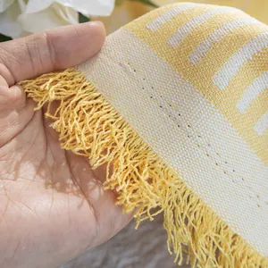 Detail of yellow and white woven cotton sofa cover with decorative tassel fringe edges