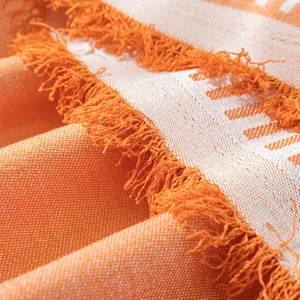 Detail view of orange and white woven cotton linen fabric with delicate fringe tassels