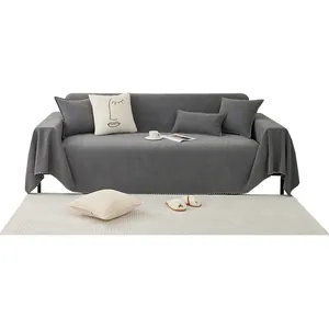 Dark gray woven sofa cover with decorative white tassel fringe in a cozy home setting