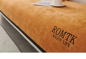 Détail d'une housse de canapé en chenille orange avec broderie et bordure noire passepoilée
