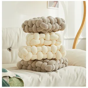 Gros plan de coussins nœuds tressés main en gris et crème sur un canapé moelleux