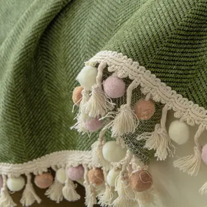 Green chenille sofa cover with herringbone pattern and decorative pompom fringe