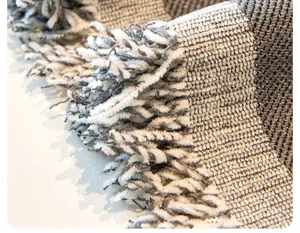 Detailed close-up of gray and beige reversible sofa cover with soft woven tassel fringe