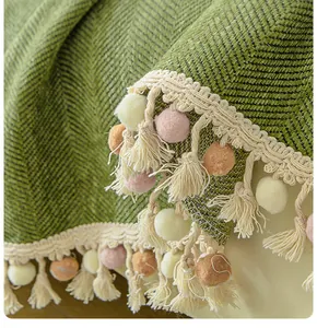 Detailed close-up of green herringbone chenille sofa cover with soft tassels and colorful pom-poms