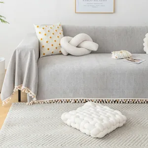 Light gray herringbone chenille sofa cover with decorative tassels and textured pillows