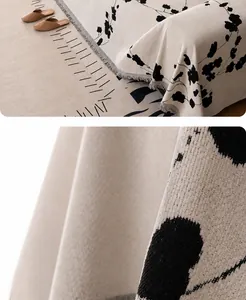 Detail of woven beige chenille sofa cover with black floral patterns and tassel fringe