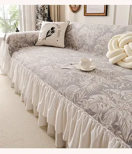 Detail of grey chenille sofa cover with tropical leaf prints and white ruffled skirt edges