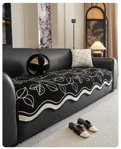 Detail of chenille sofa cover with black leaf pattern and wave-shaped edges on leather sofa
