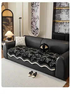 Detail of chenille sofa cover with leaf embroidery and wavy edges on a black leather sofa